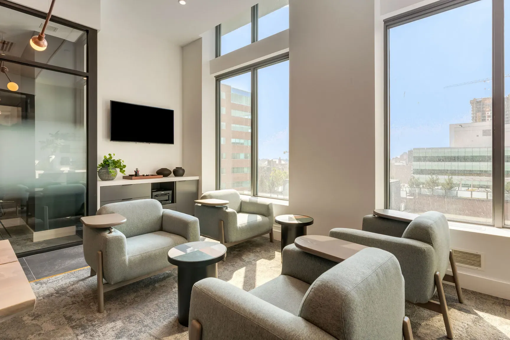 Modern lounge area with light grey armchairs, a large flat-screen TV, and bright windows.
