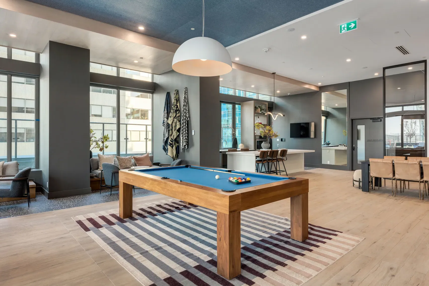 Modern common room featuring a pool table, lounge area, and bar with large windows.