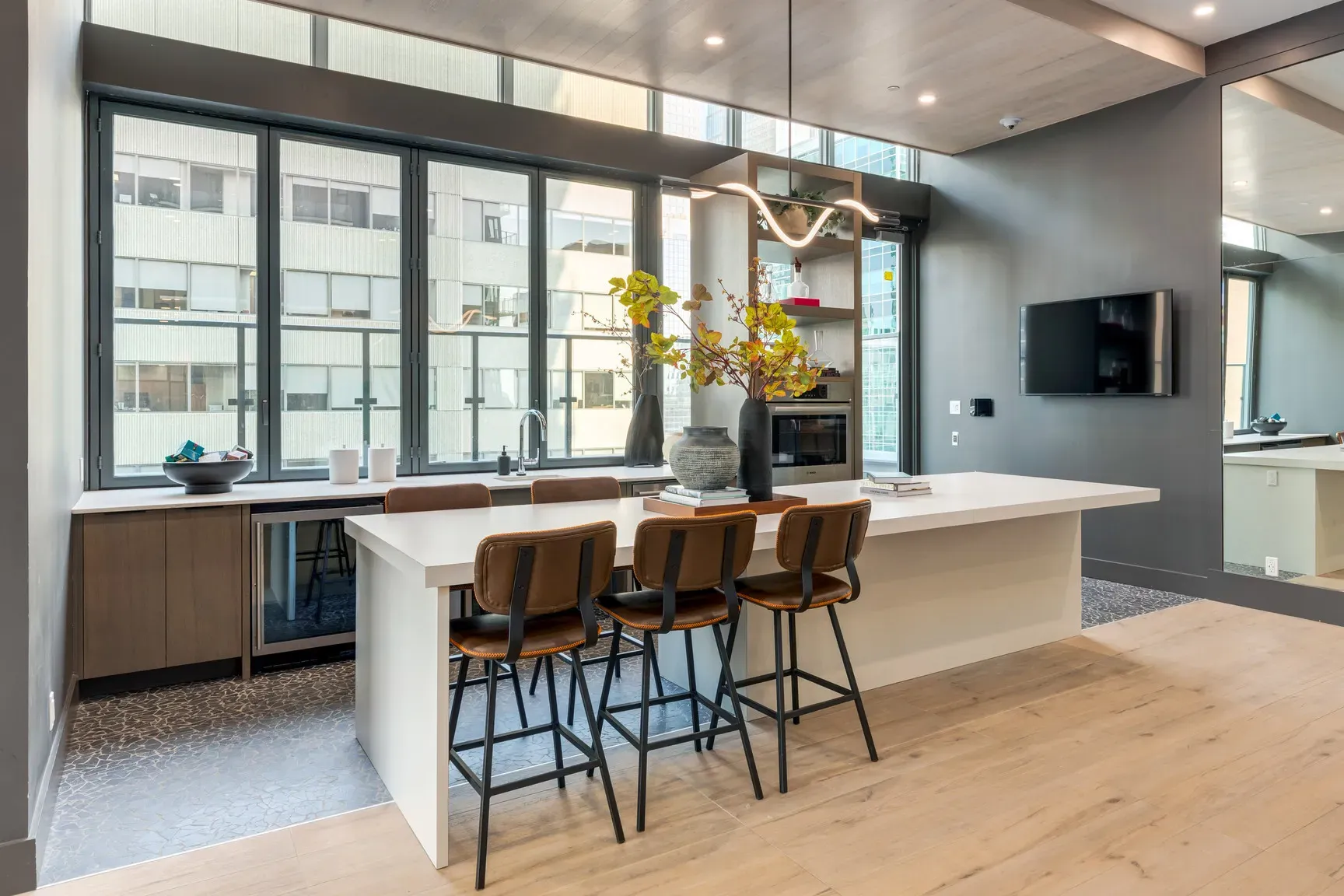 Modern kitchen with a white island, three bar stools, and a sink beneath large windows.
