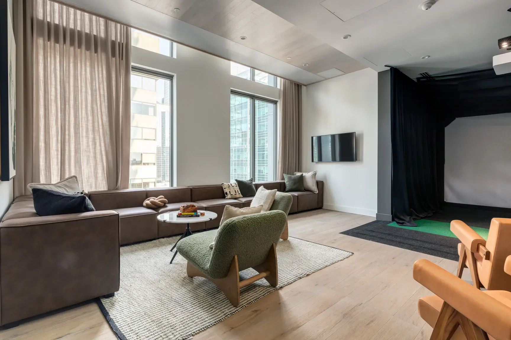 Modern living room with a brown L-shaped sofa, green armchair, and a golf simulator area.