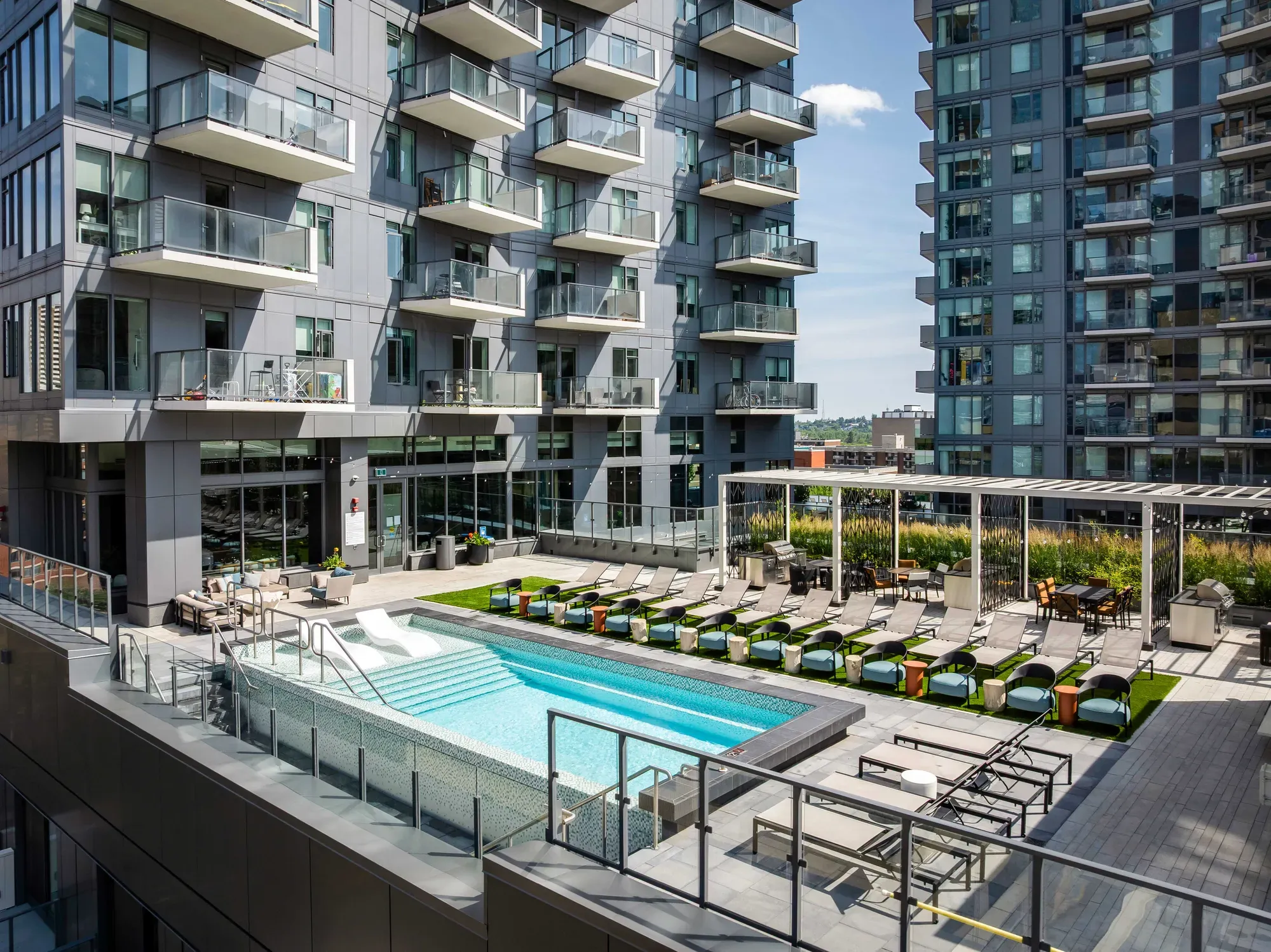 Modern apartment complex with a rooftop swimming pool and numerous lounge chairs on an amenity deck.